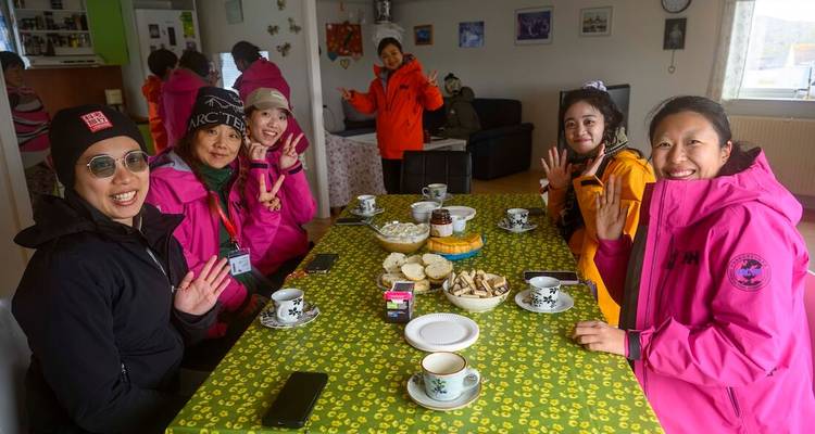 Groupe de voyageurs en vestes colorées savourant café et gâteaux autour d'une table de cuisine.