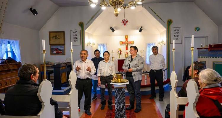 Une chorale locale se produit dans une petite église de village arctique éclairée aux bougies pendant que des visiteurs regardent.