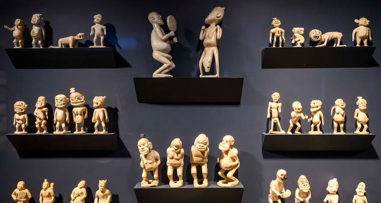 Mur d'exposition de figurines inuites sculptées disposées sur des étagères noires dans un musée.