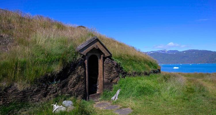 Petite entrée de hutte en pierre au toit de tourbe située dans une colline herbeuse au bord d'un fjord bleu.