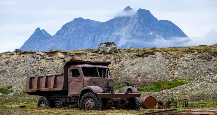 Camion à benne rouillé abandonné dans un paysage arctique rocheux avec des montagnes spectaculaires.