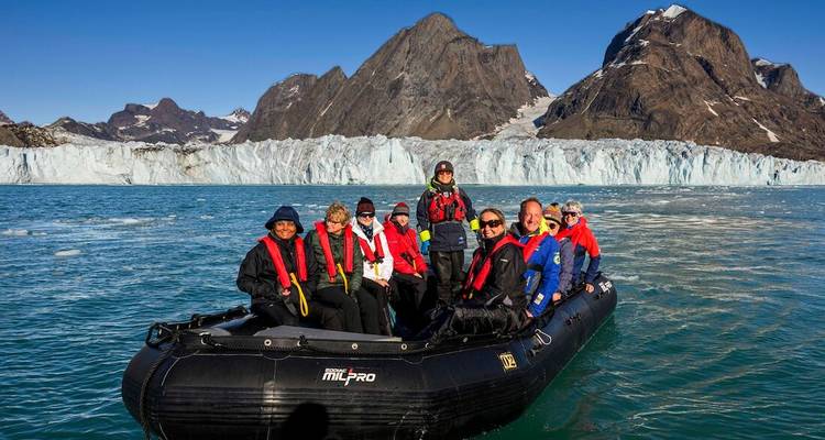 Groupe de touristes dans un bateau pneumatique rigide noir portant des gilets de sauvetage avec un mur de glacier et des pics acérés en arrière-plan.