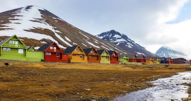 Rangée de maisons en bois aux couleurs vives disposées contre des pentes de toundra aride et des sommets enneigés à Longyearbyen.