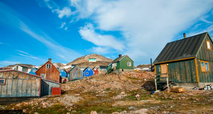 Des maisons en bois colorées éparpillées sur une colline rocheuse du Groenland sous un ciel bleu éclatant.