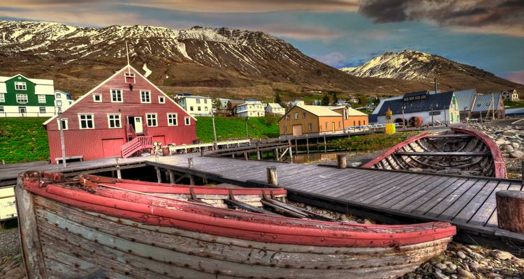 Edificios de madera coloridos y viejos barcos de pesca contra montañas cubiertas de nieve durante la cálida luz del atardecer.