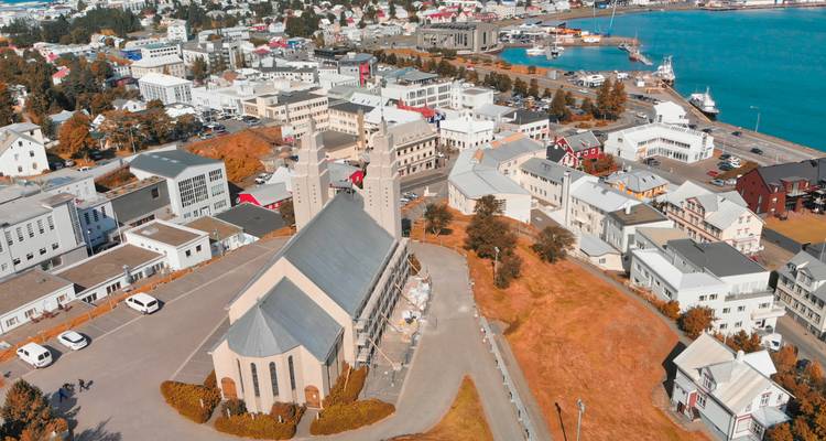 Vista aérea de Akureyri con su iglesia prominente, casas circundantes y puerto turquesa en un día despejado.