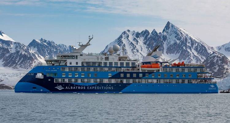 Barco de crucero de expedición azul anclado ante dramáticos picos nevados.