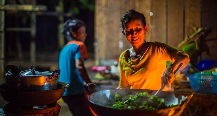 Femme souriante faisant sauter des légumes verts à feu vif dans une cuisine rustique le soir