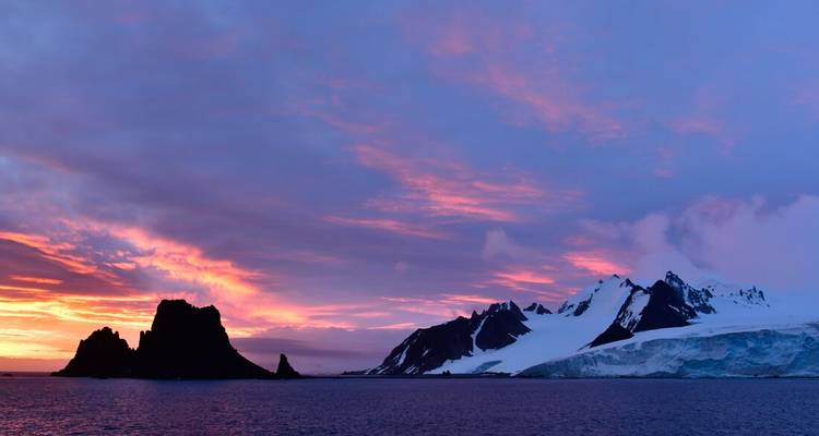 Lebendiger rosa und violetter Sonnenuntergang über schneebedeckten antarktischen Gipfeln und dunklem Meer.