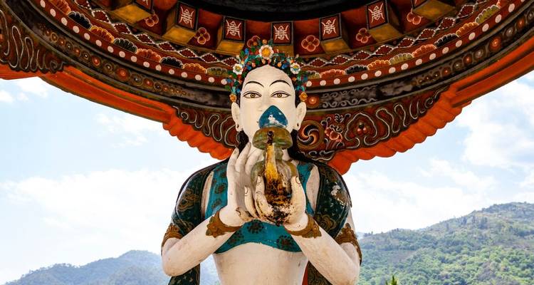 Statue bouddhiste bhoutanaise colorée tenant une conque sous un toit de temple peint.