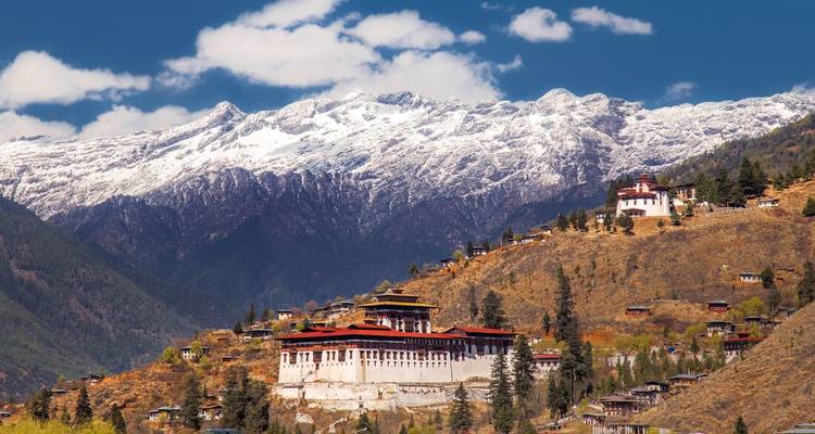La forteresse de Paro Dzong domine une colline en terrasses avec les Himalayas couronnés de neige en arrière-plan.