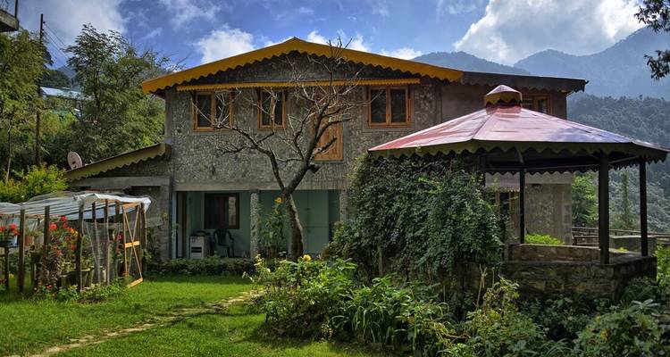 Maison d'hôtes rustique en pierre avec jardin et tonnelle située contre les collines boisées bhoutanaises.
