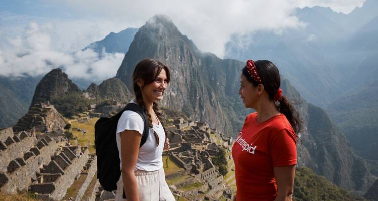 Deux voyageurs partagent un sourire au sommet du Machu Picchu avec les pics brumeux des Andes qui s'élèvent de façon spectaculaire derrière les ruines.