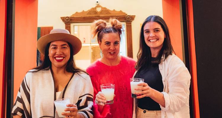 Trois femmes souriantes tiennent des boissons péruviennes traditionnelles en posant à l'intérieur.