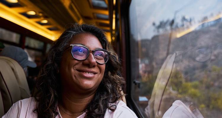 Une femme contemple avec contentement par la fenêtre d'un train pittoresque tandis que les paysages andins défilent.