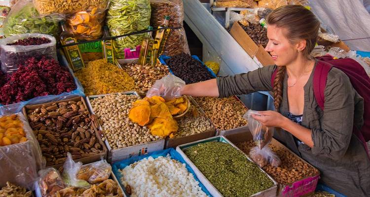 Un voyageur sélectionne des fruits secs colorés et des noix à un étal de marché local vibrant.