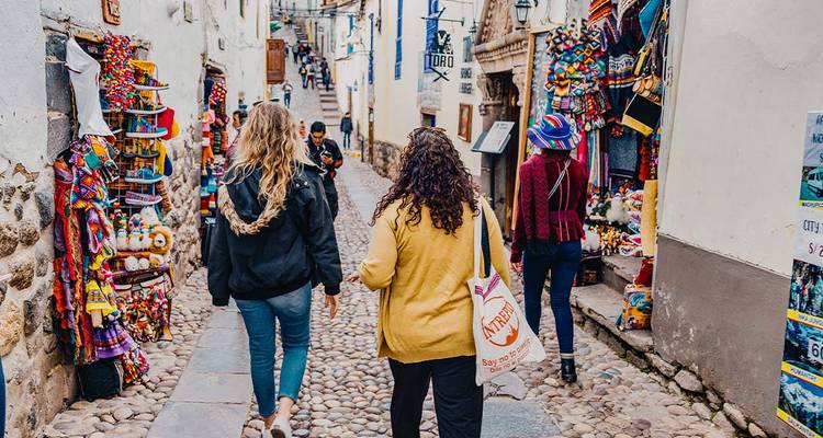 Les voyageurs marchent le long d'une ruelle pavée étroite bordée d'étals d'artisanat colorés et de murs d'adobe blanchis à la chaux.