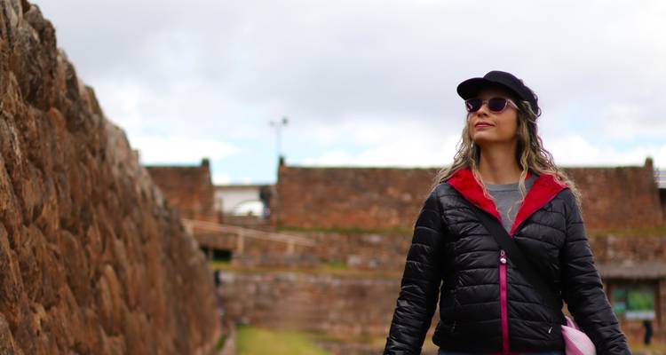 Une femme en veste noire lève les yeux à côté des murs de pierre inca massifs d'une ancienne forteresse.