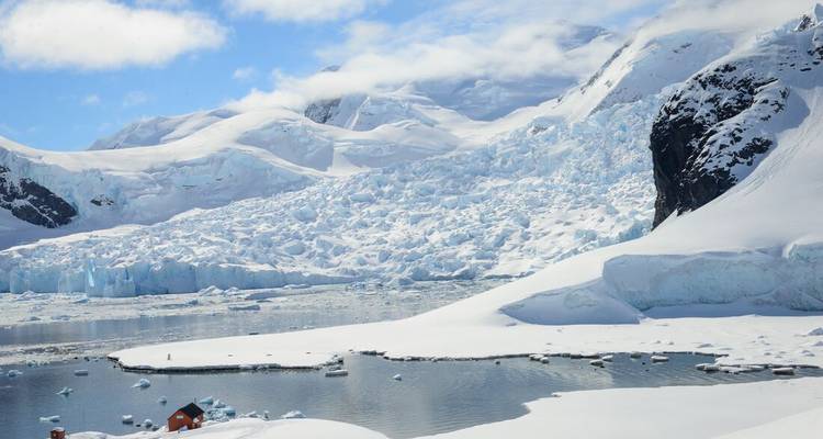 Weite antarktische Landschaft mit schneebedeckten Bergen und einem kalbenden Gletscher, der auf eine ruhige Bucht trifft.