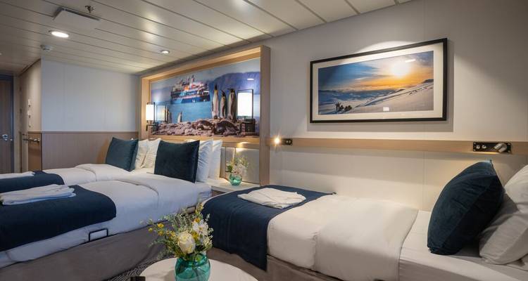 Modern twin-bed cruise ship cabin with nautical artwork, soft lighting, and fresh flowers on a table.