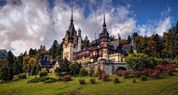 Märchenschloss Peleș umgeben von herbstlichem Wald unter dramatischen Wolken