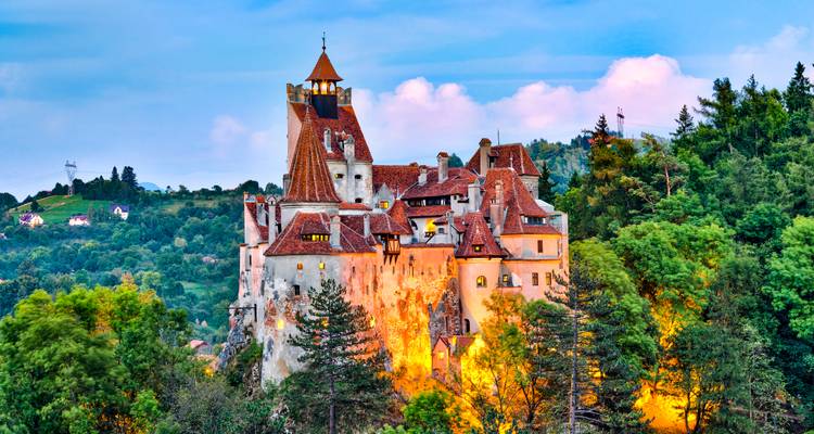 Château emblématique de Bran au sommet d'une colline boisée éclairé chaleureusement contre le ciel du soir