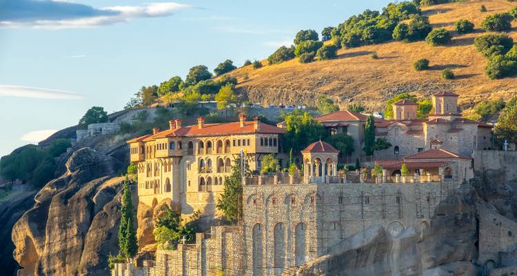 Un monasterio bañado por el sol encaramado sobre los imponentes pilares rocosos de Meteora en medio de la luz dorada del atardecer y acantilados escarpados.