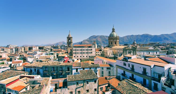 Vista despejada desde la azotea de las cúpulas barrocas y tejados de terracota de Palermo contra las montañas distantes.