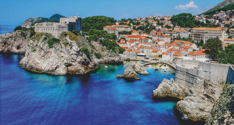 Dramática vista aérea del casco antiguo amurallado de Dubrovnik encaramado en acantilados rocosos sobre las vívidas aguas turquesas del Adriático.