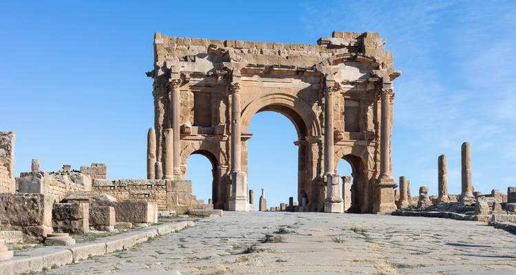 Imposing Arch of Trajan standing at the entrance to Roman ruins beneath a clear blue sky
