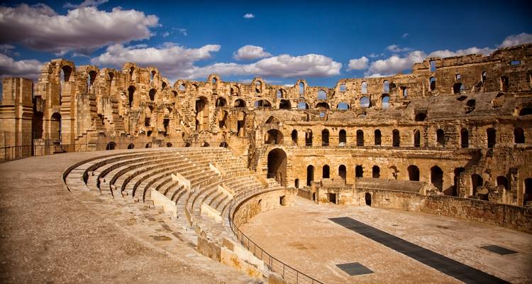 Interior panorama of the vast stone seating tiers inside the El Jem Roman amphitheatre under a blue sky