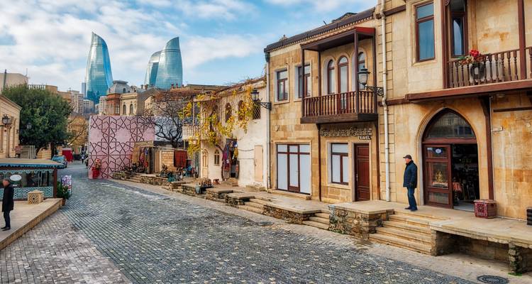 Kopfsteinpflasterstraße in der Altstadt von Baku mit historischen Häusern und den modernen Flame Towers im Hintergrund.