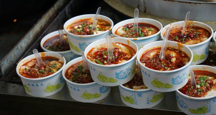 Stacks of spicy noodle soup bowls topped with chili oil and herbs at a street food stall.