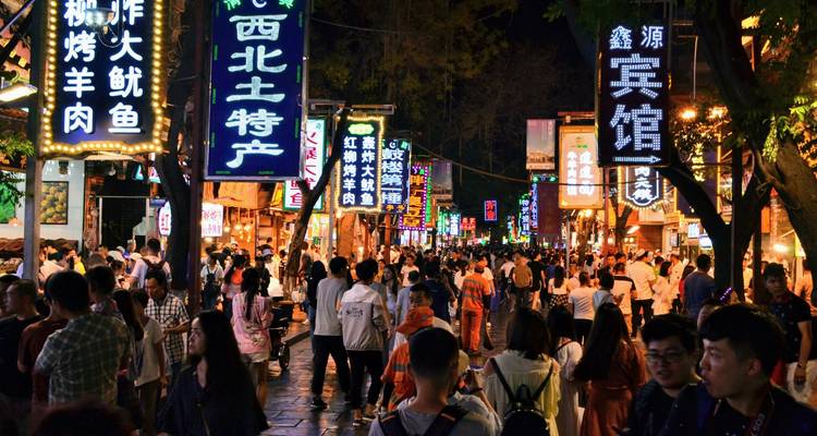 A bustling night market street glows with colourful neon signs and crowds of shoppers.