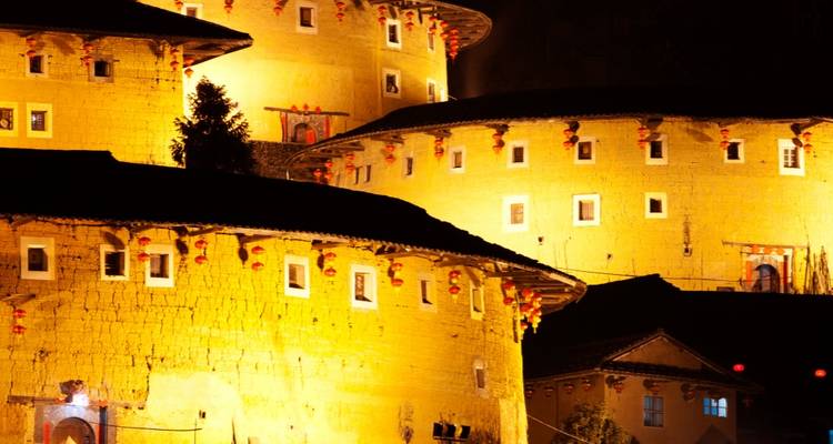Forteresses circulaires traditionnelles en terre illuminées chaleureusement contre le ciel nocturne.