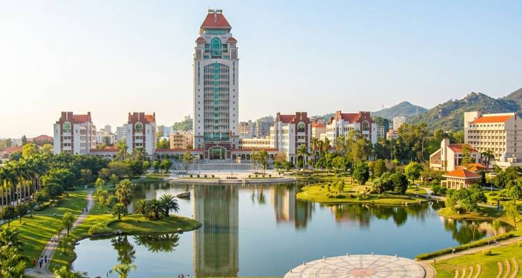 Campus moderne au bord du lac avec une haute tour centrale reflétée dans l'eau tranquille et des jardins entretenus.