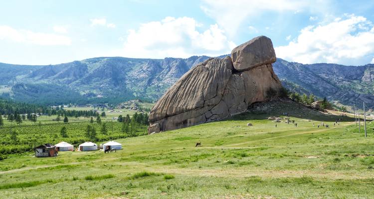 Formation rocheuse emblématique de Turtle Rock se dressant au-dessus de prairies vertes parsemées de yourtes traditionnelles mongoles et de visiteurs.
