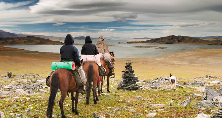 Cavaliers avec des paquetages surplombant un vaste lac et une steppe sous des nuages dramatiques.