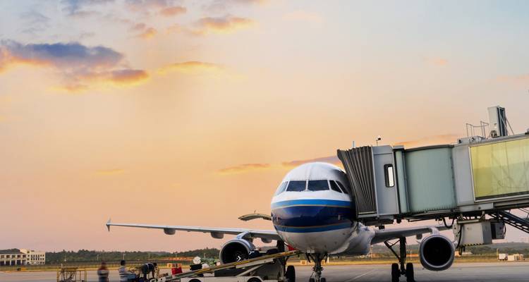 Commercial jet connected to a jet bridge during a pastel sunset sky.