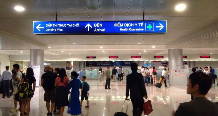 Arriving passengers walk beneath bilingual arrival and health-quarantine signs inside the terminal.