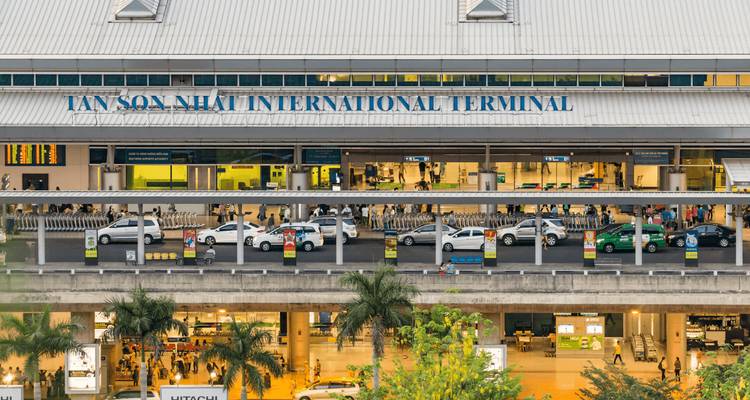 Wide view of Tan Son Nhat International Terminal with taxi queues and palm trees.