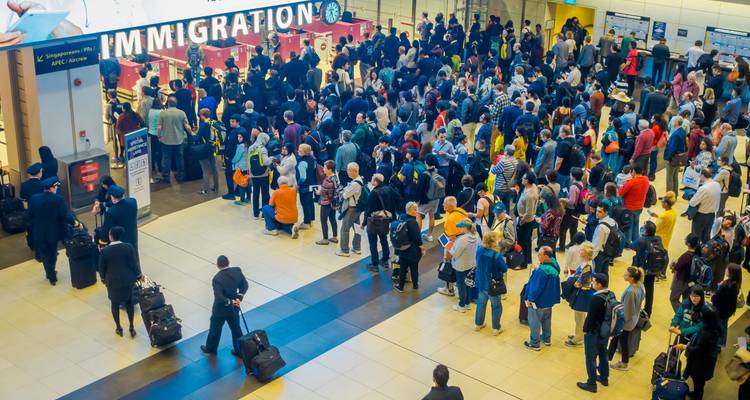 Heavy crowd of travellers forms a long immigration queue beneath bright signage.
