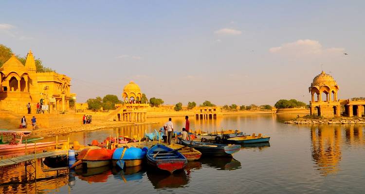 Des bateaux colorés reposent sur le lac Gadisar entouré de chhatris en grès jaune qui brillent dans la lumière du soir.