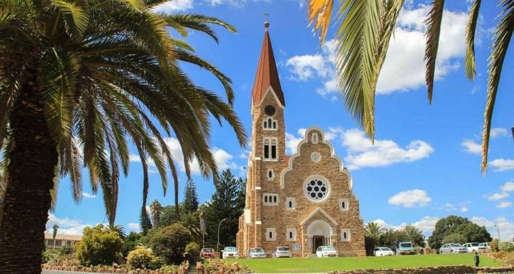 Vue au niveau du sol de l'historique Christuskirche encadrée par des palmiers et un ciel bleu