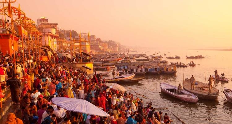 Menigten verzamelen zich bij de ghats van Varanasi langs de Ganges terwijl boten de rivier omsäumen bij zonsopgang.