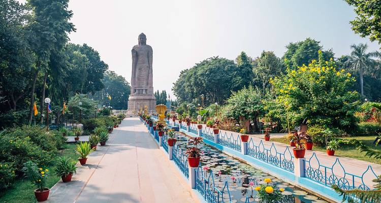 Een hoge staande Boeddhabeeld rijst op aan het einde van een verzorgd tuinpad omzoomd met lelienvijvers.