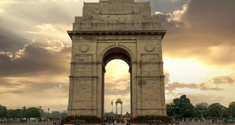 Monument majestueux d'India Gate silhouetté par des nuages dorés dramatiques et les rayons de fin d'après-midi.