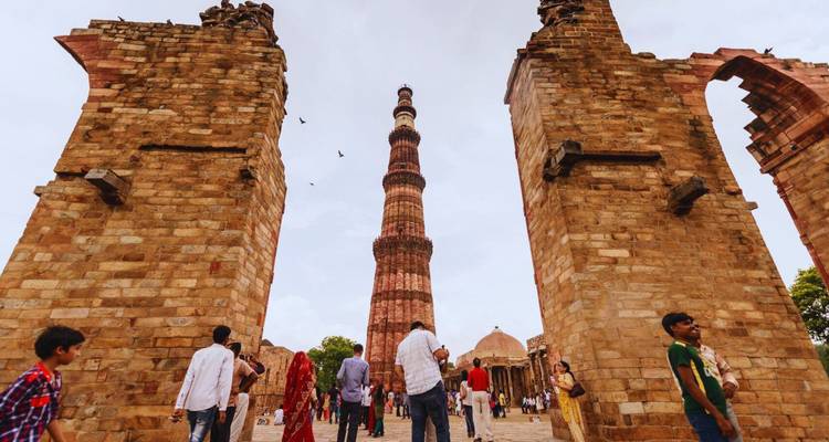 Les visiteurs marchent à travers des arches de grès encadrant la tour élancée de Qutub Minar.