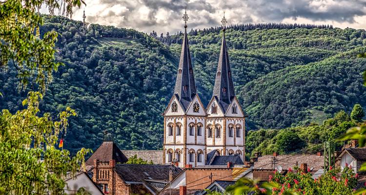 Kerk met twee torens die oprijst boven een schilderachtig stadje in de Rijndal, omgeven door beboste heuvels.