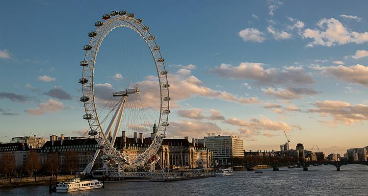 Het London Eye dat boven de Theems uittorent met warme zonsondergangwolken.